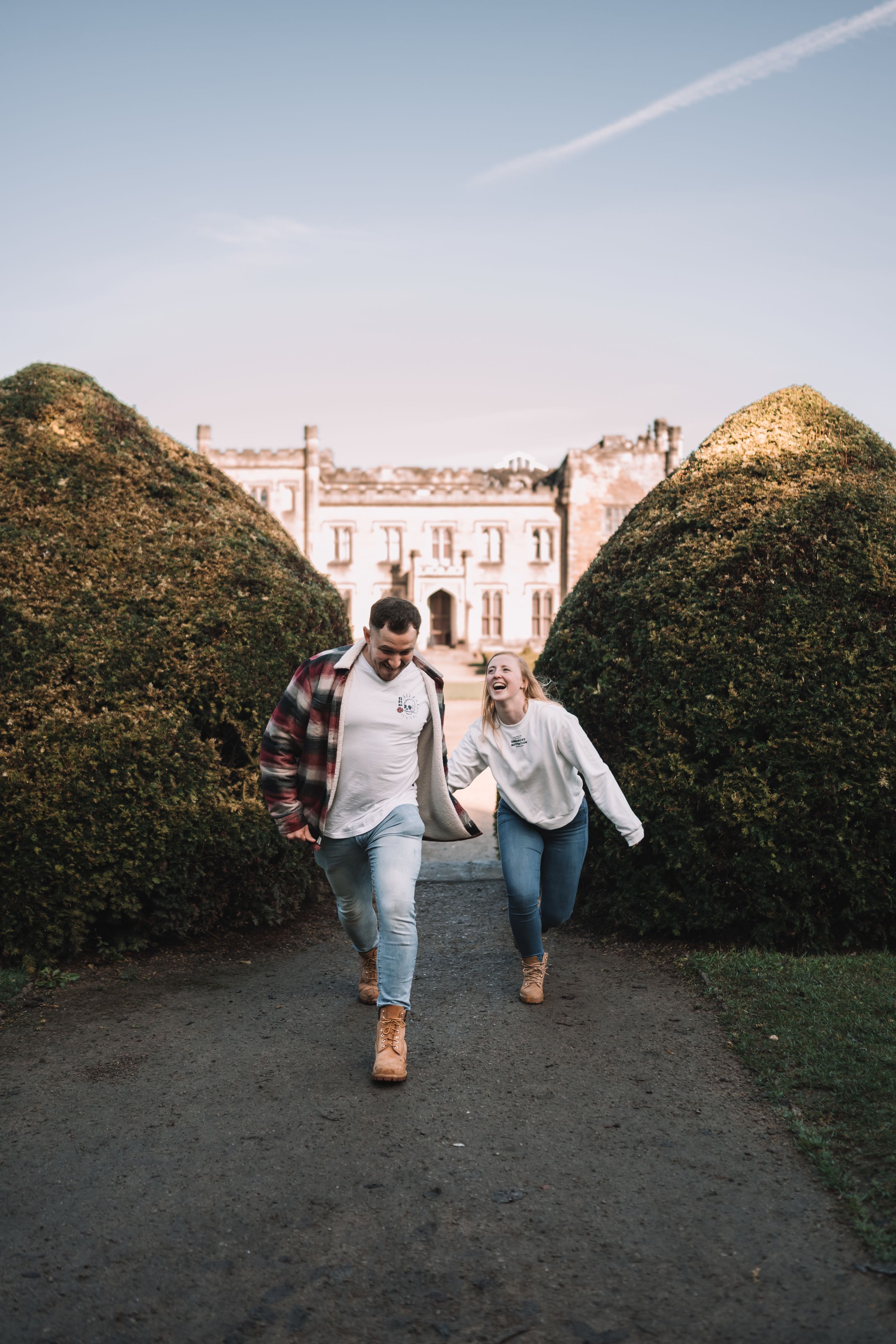 Two people walking together on a path between tall hedges with a grand building visible in the background.
