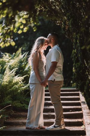 A romantic moment captured between a couple in white attire standing on garden steps surrounded by lush greenery.