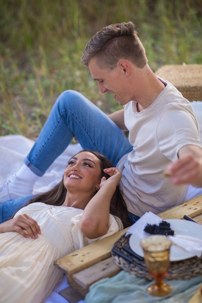 A couple enjoys a relaxing picnic date outdoors on a wooden board while lying down together.