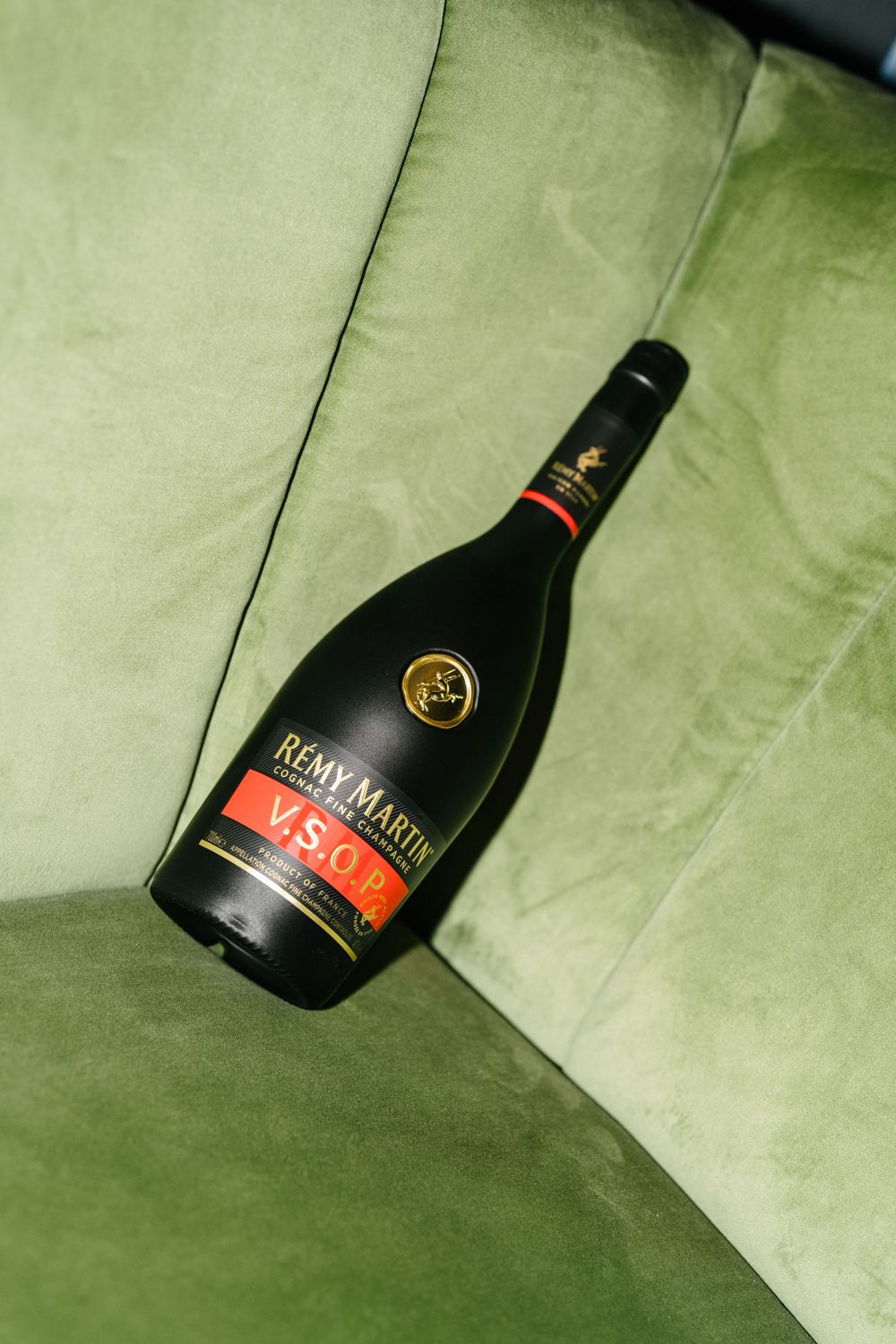 A bottle of Remy Martin 1738 cognac resting on a plush green velvet couch or chair surface.