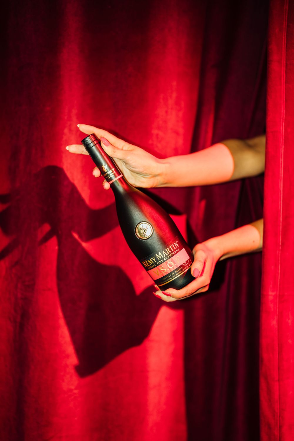 Hands holding a red bottle of Moet & Chandon champagne against a dramatic red velvet curtain backdrop.
