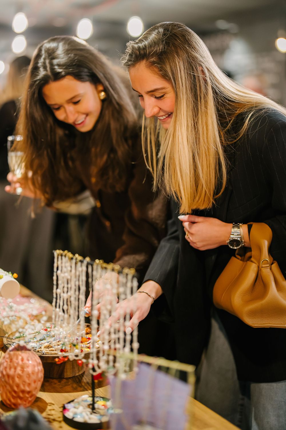 Two friends in black outfits share a joyful moment while browsing jewelry at a retail display with festive decorations.