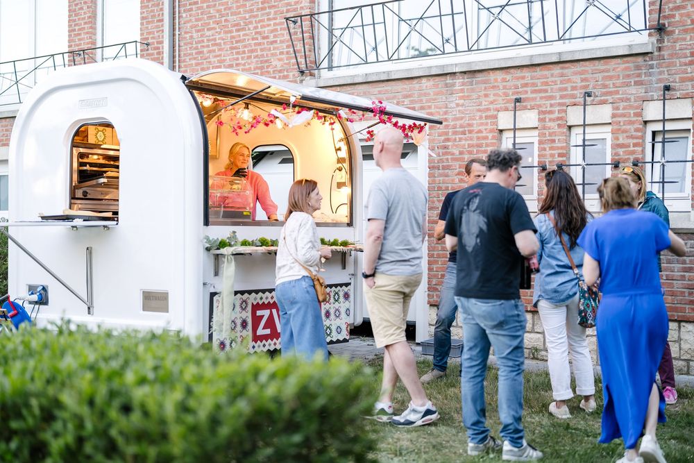 People wait in line outside a brick building entrance during a community event.