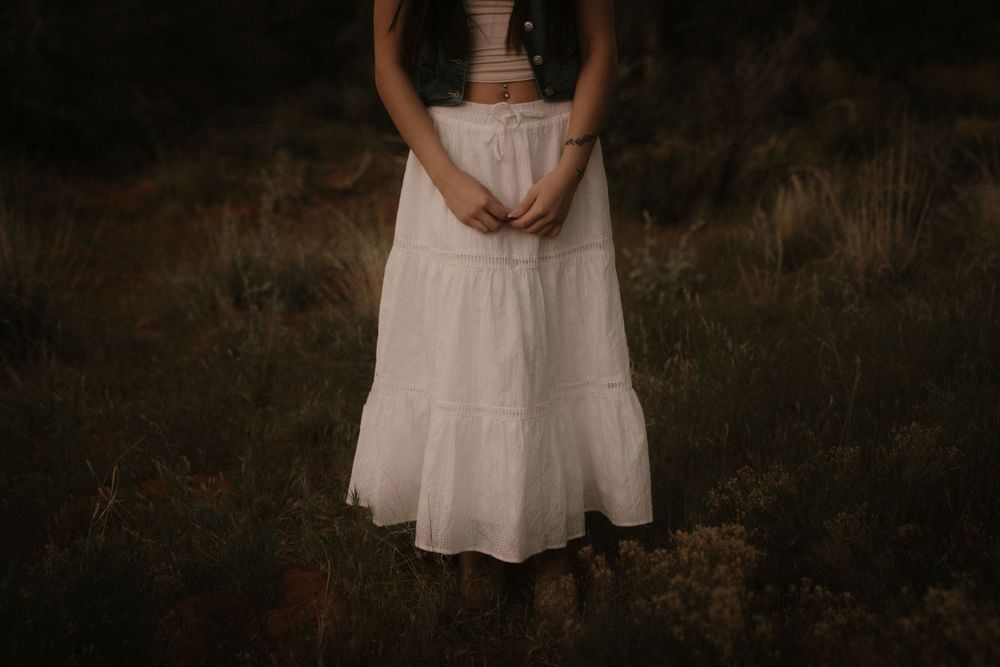 Cropped view of white ruffled skirt against dark natural backdrop in moody lighting.
