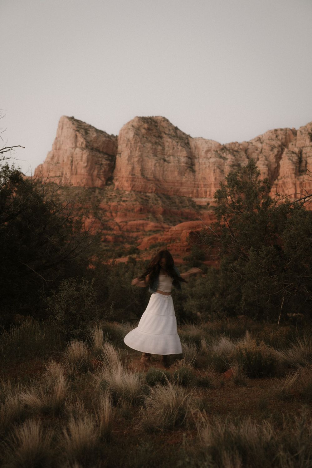 Dancing figure in white dress against dramatic red rock cliffs at dusk.