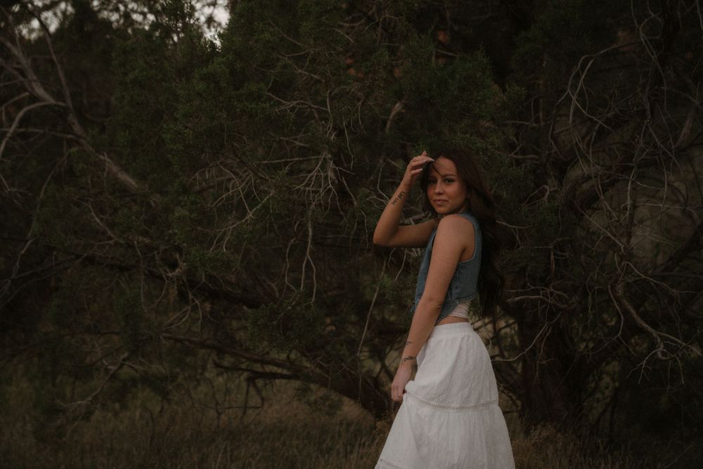 Artistic portrait in a rustic setting with white flowing skirt and dark top at dusk.