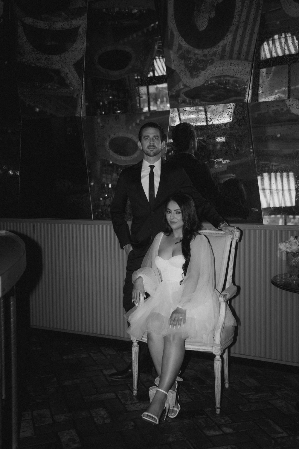 A formal couple poses in an elegant venue with mirrored wall details and moody lighting.