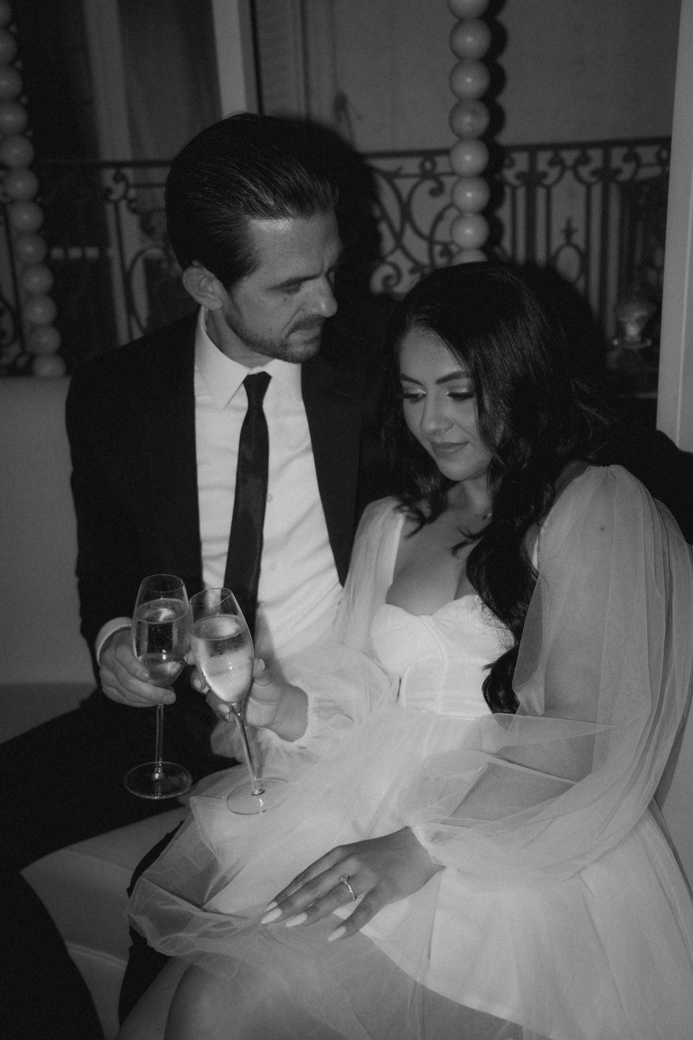 A couple shares champagne and conversation in formal attire at an elegant venue.