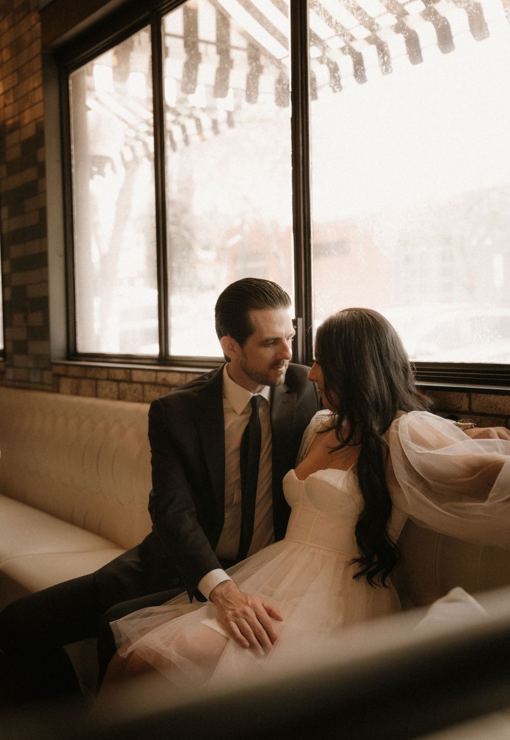 A couple shares an intimate moment on a leather couch by a large window.