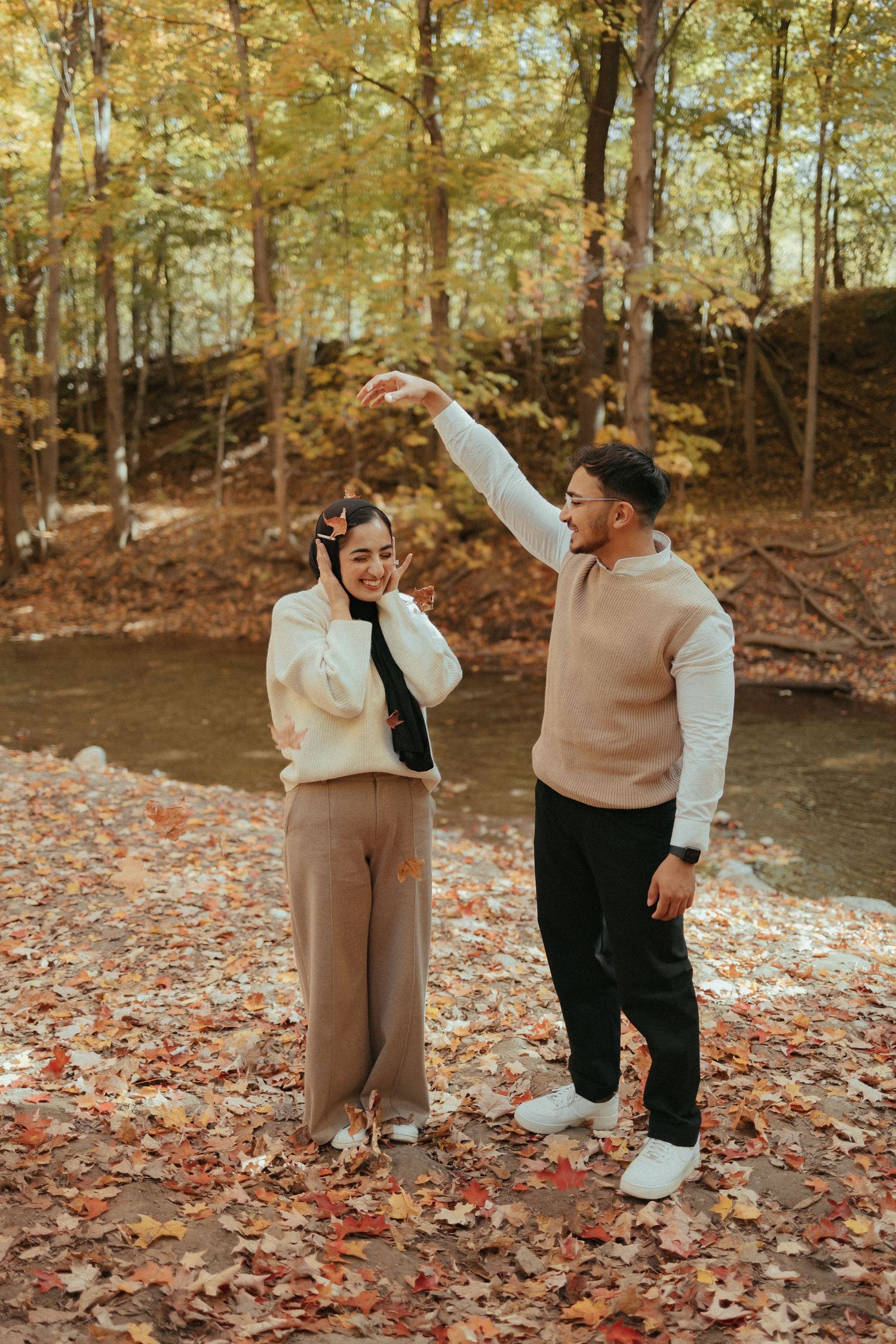 Playful autumn photoshoot showing couple in casual wear by a creek.