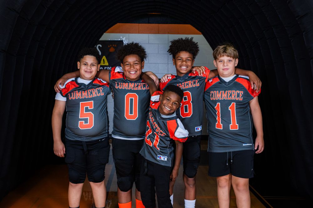 Youth football teammates in black and orange uniforms pose together in a dark tunnel.