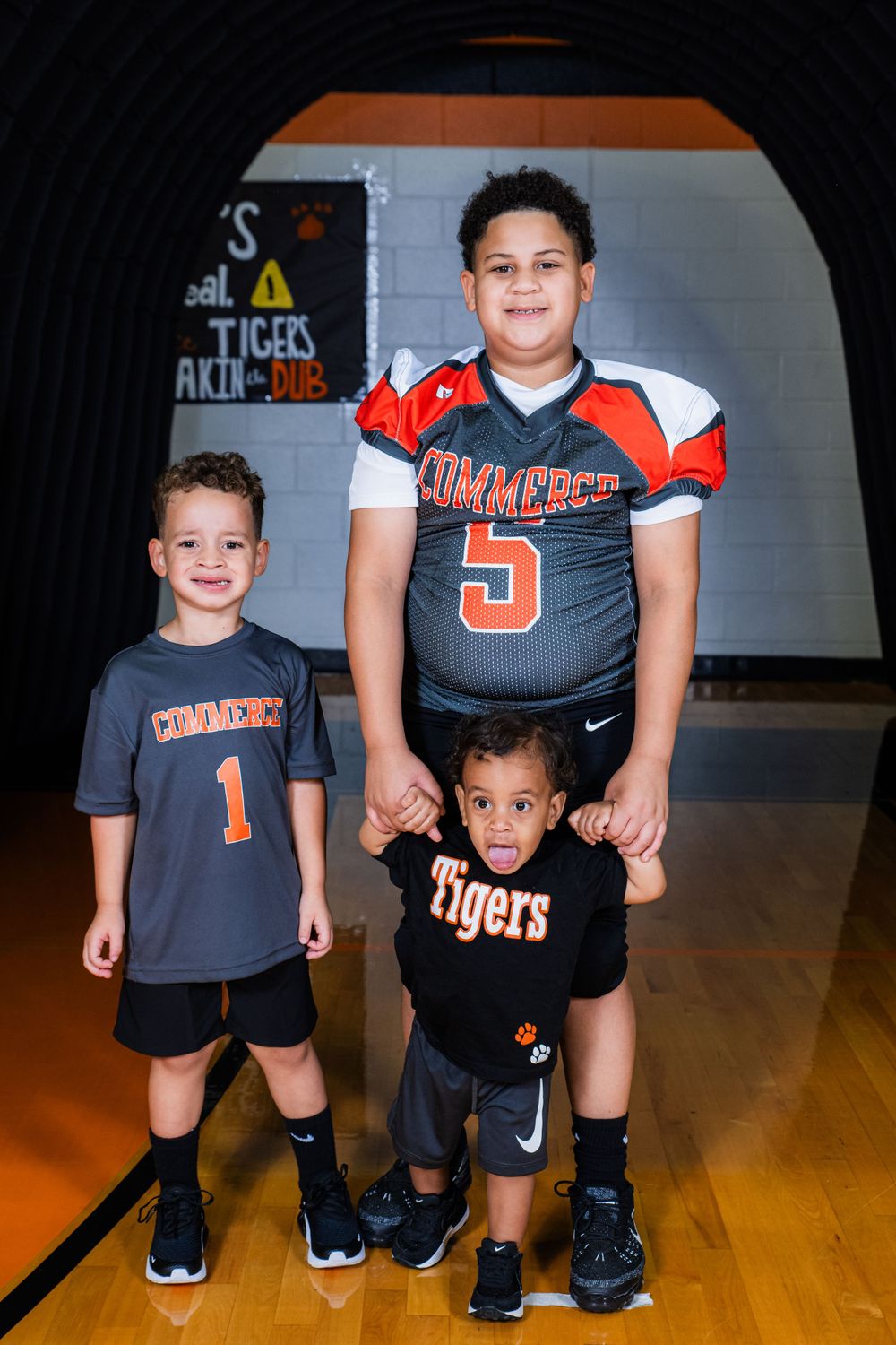 Three youth athletes stand together in their Tigers team uniforms on a gymnasium floor.