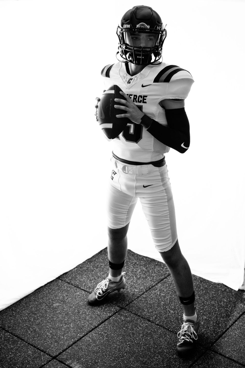 Football player in white uniform poses in dramatic black and white photo.
