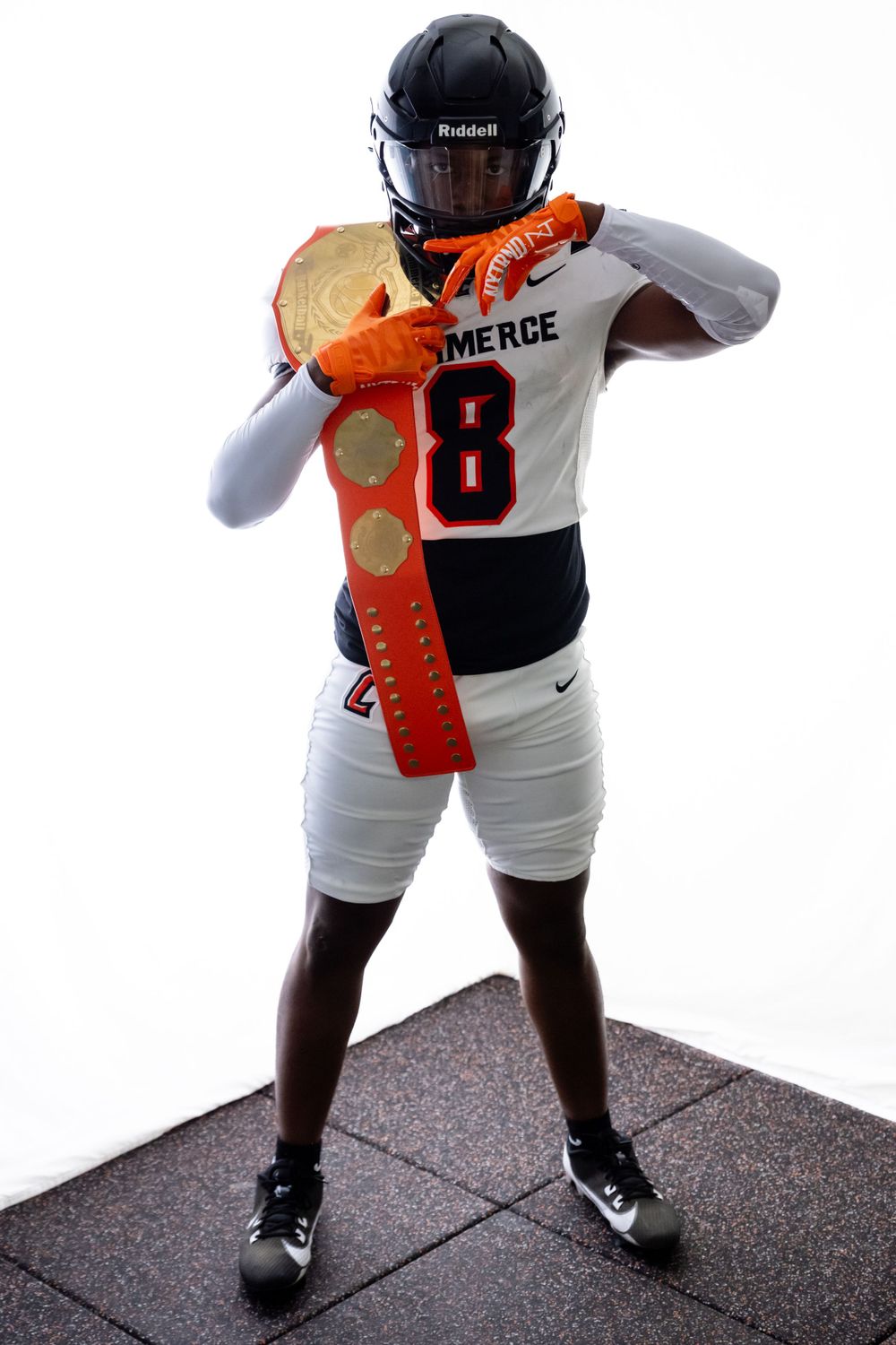Football player in black helmet, white jersey number 8, and orange gloves strikes dynamic pose during photo session.