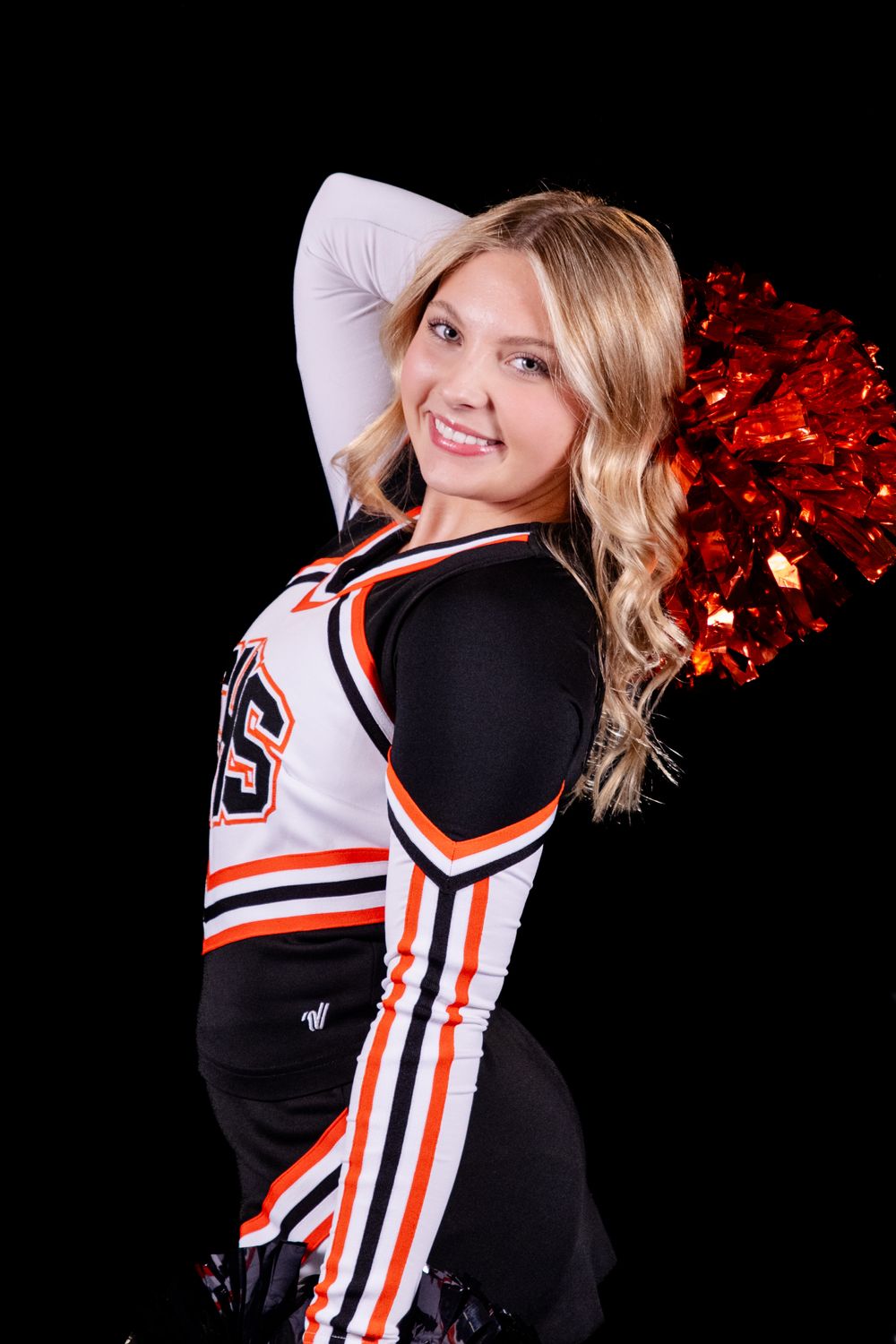 Cheerleader in black and orange uniform with red pom pom poses against dark background.