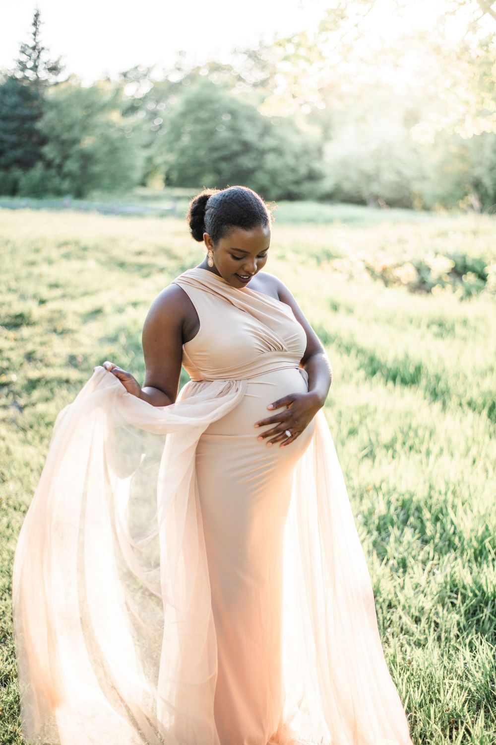 Maternity photoshoot in a flowing peach dress against a sunlit meadow background.