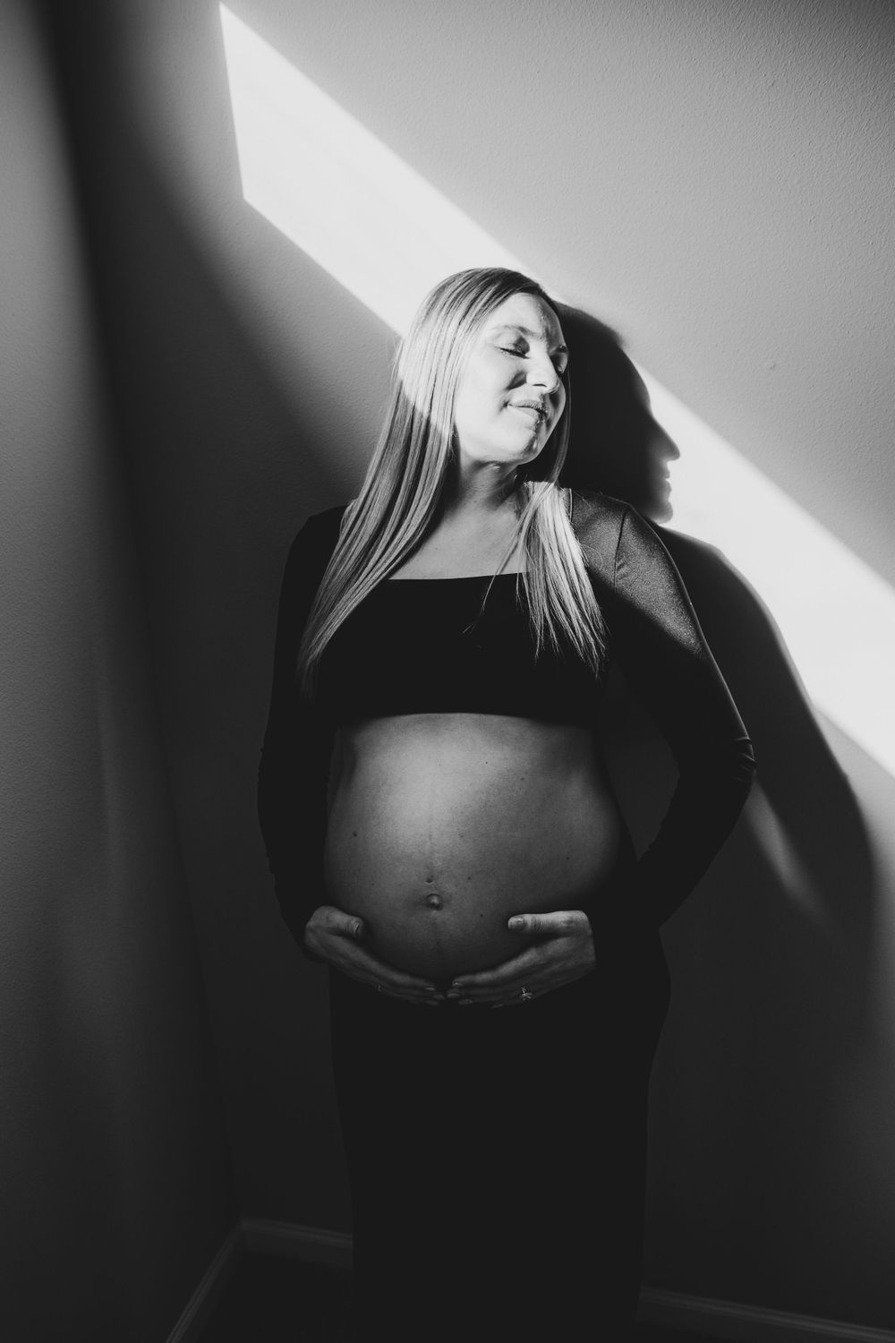 Black and white artistic maternity photo with dramatic lighting and shadows.