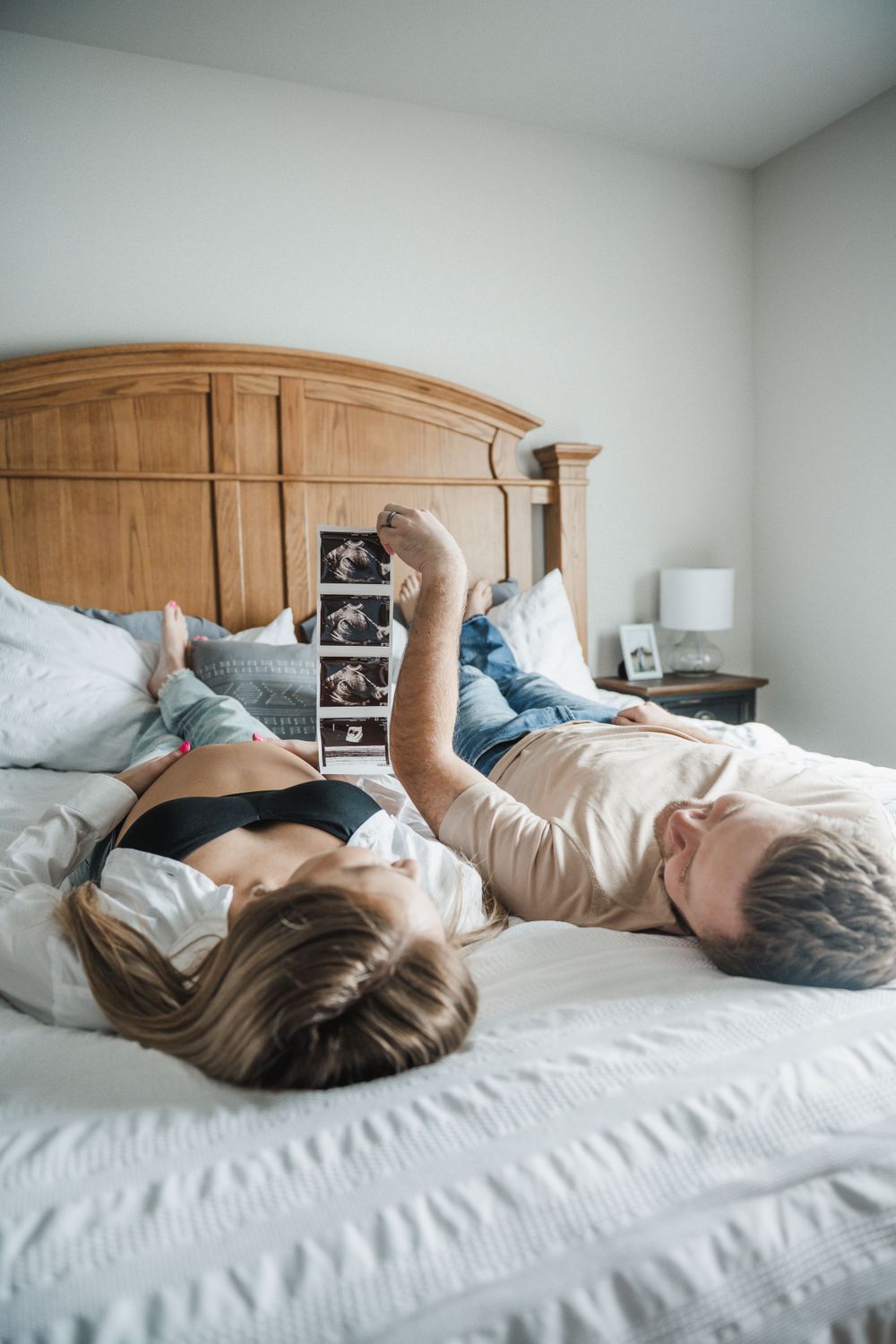 Couple lying on bed viewing ultrasound photos together in natural light.