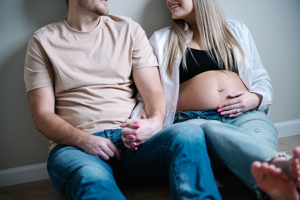 An expectant couple sits together intimately on the floor during a maternity photography session.