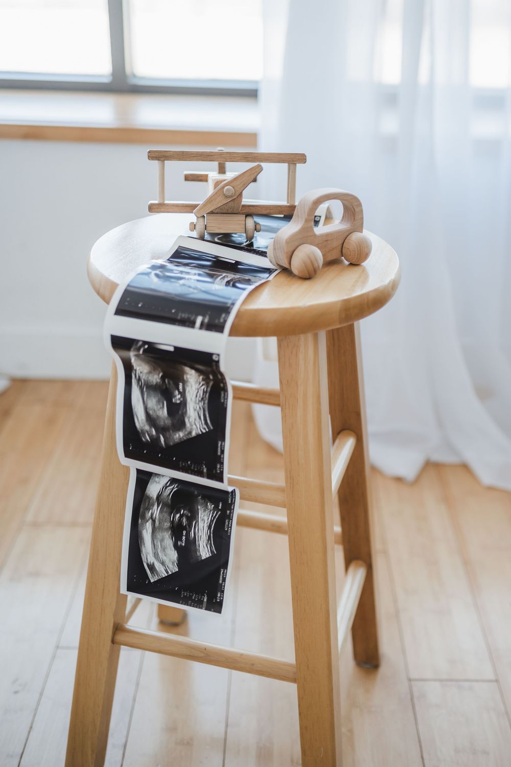 Wooden rocking chair with ultrasound photos and small plush toy in bright minimalist room.