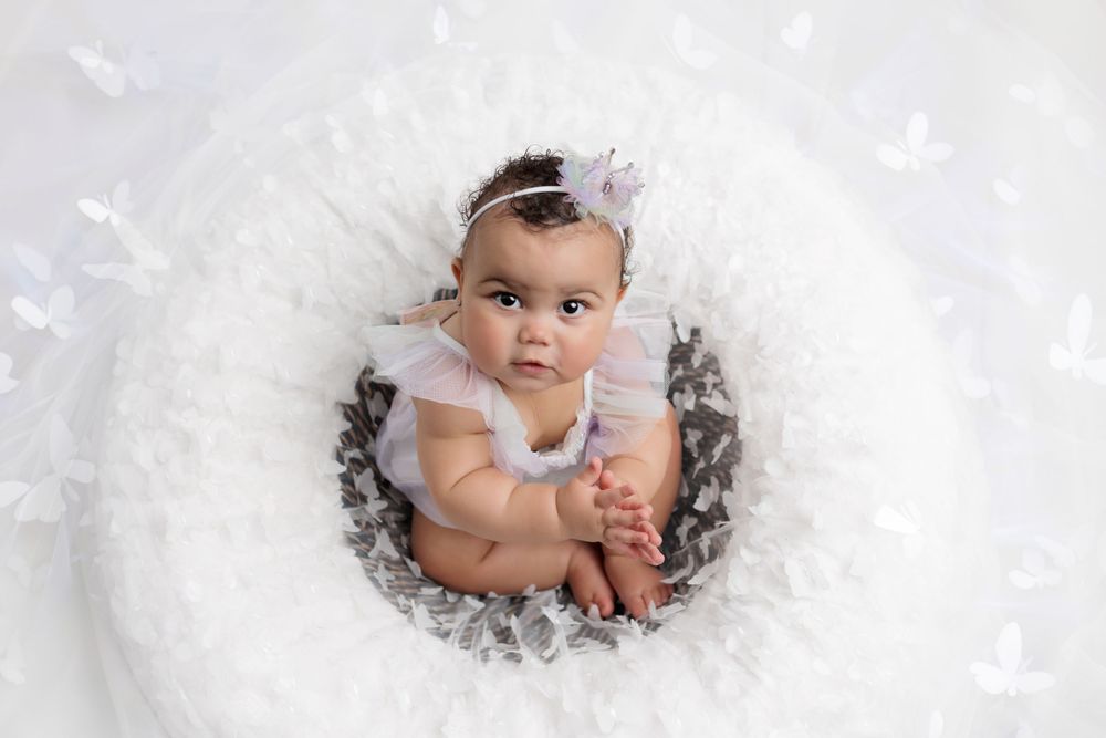 Baby sits in soft white tulle fabric surrounded by feathers during professional portrait session.
