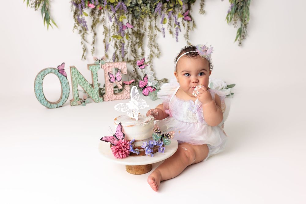 A first birthday setup with turquoise ONE letters, tea party decorations, and floral greenery hanging from above.