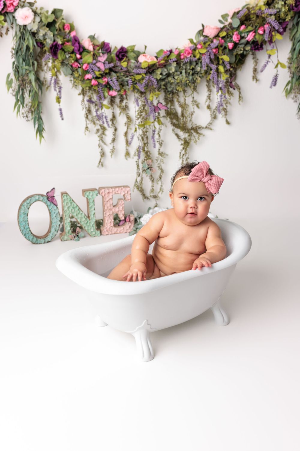 A small white clawfoot bathtub with floral decorations and mint green 'ONE' text against a white backdrop.