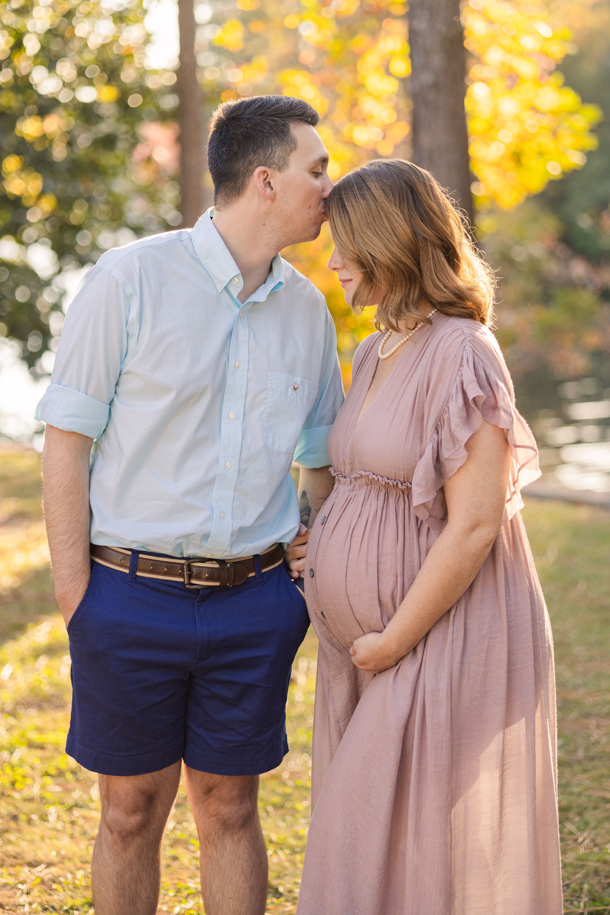 A couple shares a tender moment in a park with golden autumn foliage in the background.
