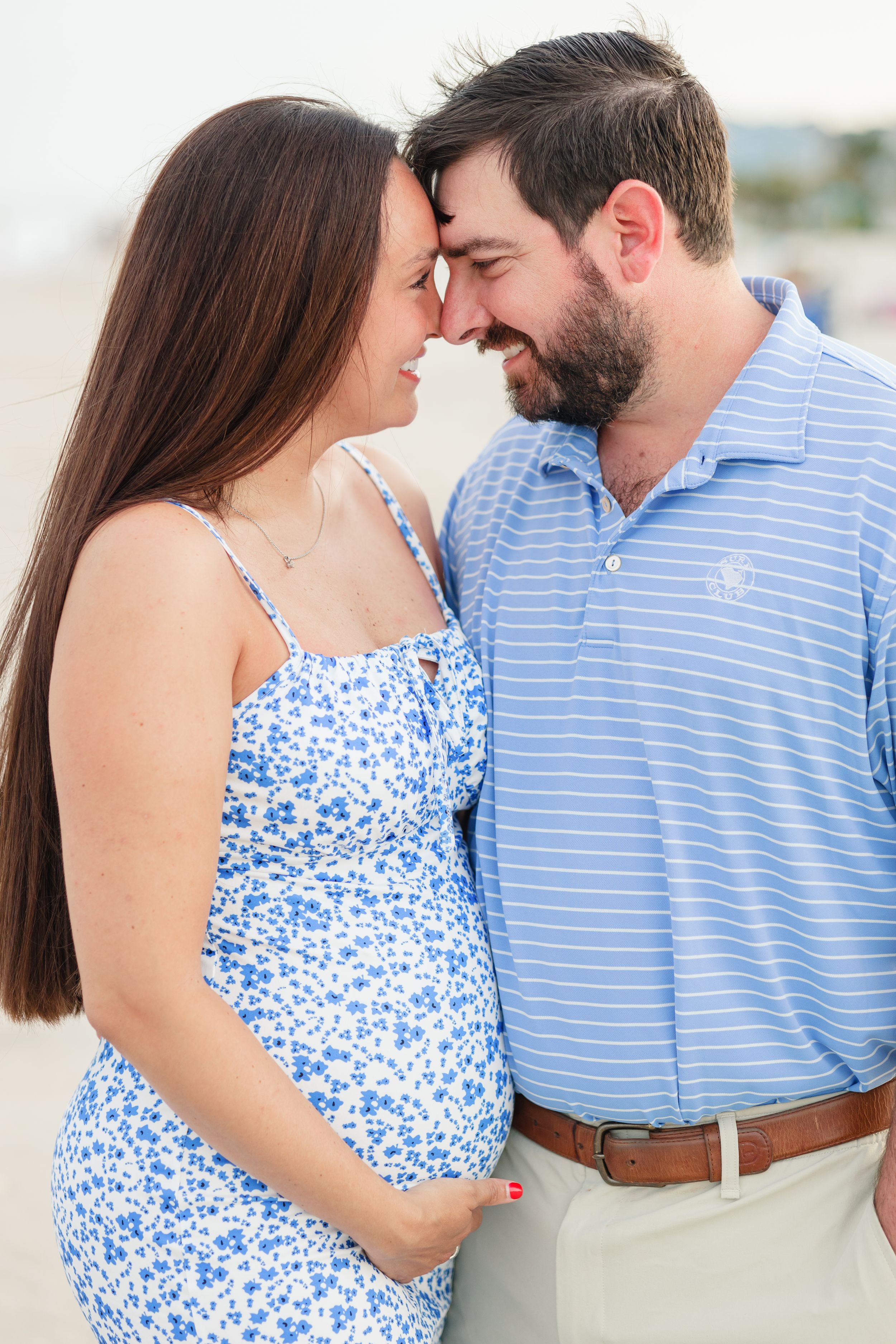 A couple in coordinating blue outfits share an intimate moment on the beach during a romantic photoshoot.