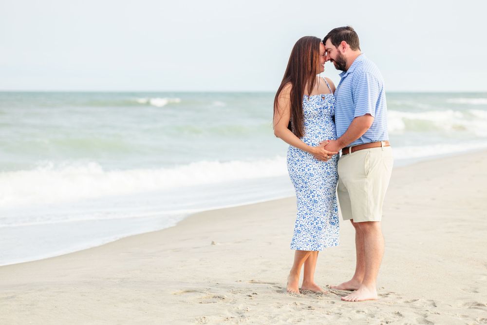 A couple walks hand in hand along a sandy beach during a romantic seaside photoshoot.