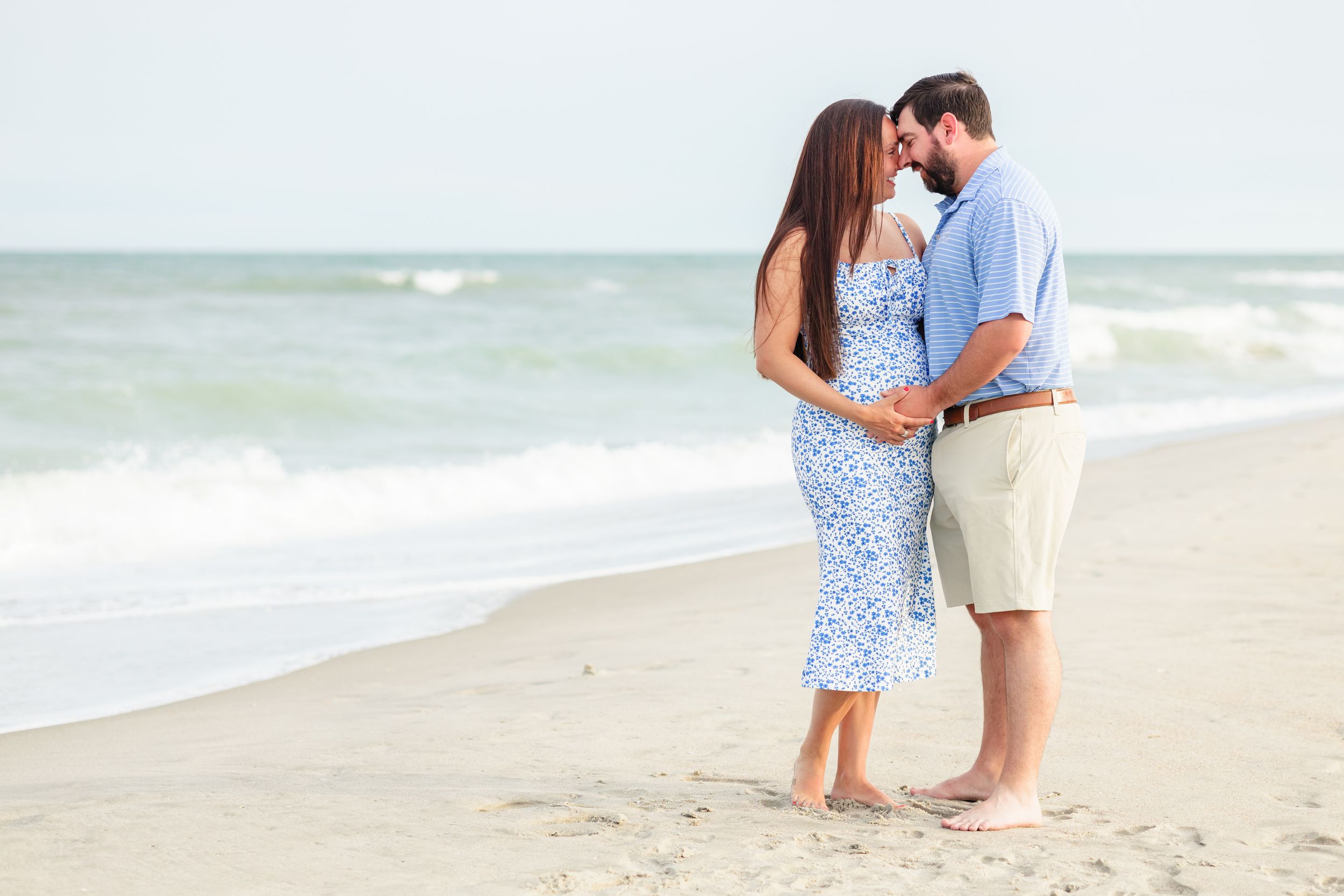A couple walks hand in hand along a sandy beach during a romantic seaside photoshoot.