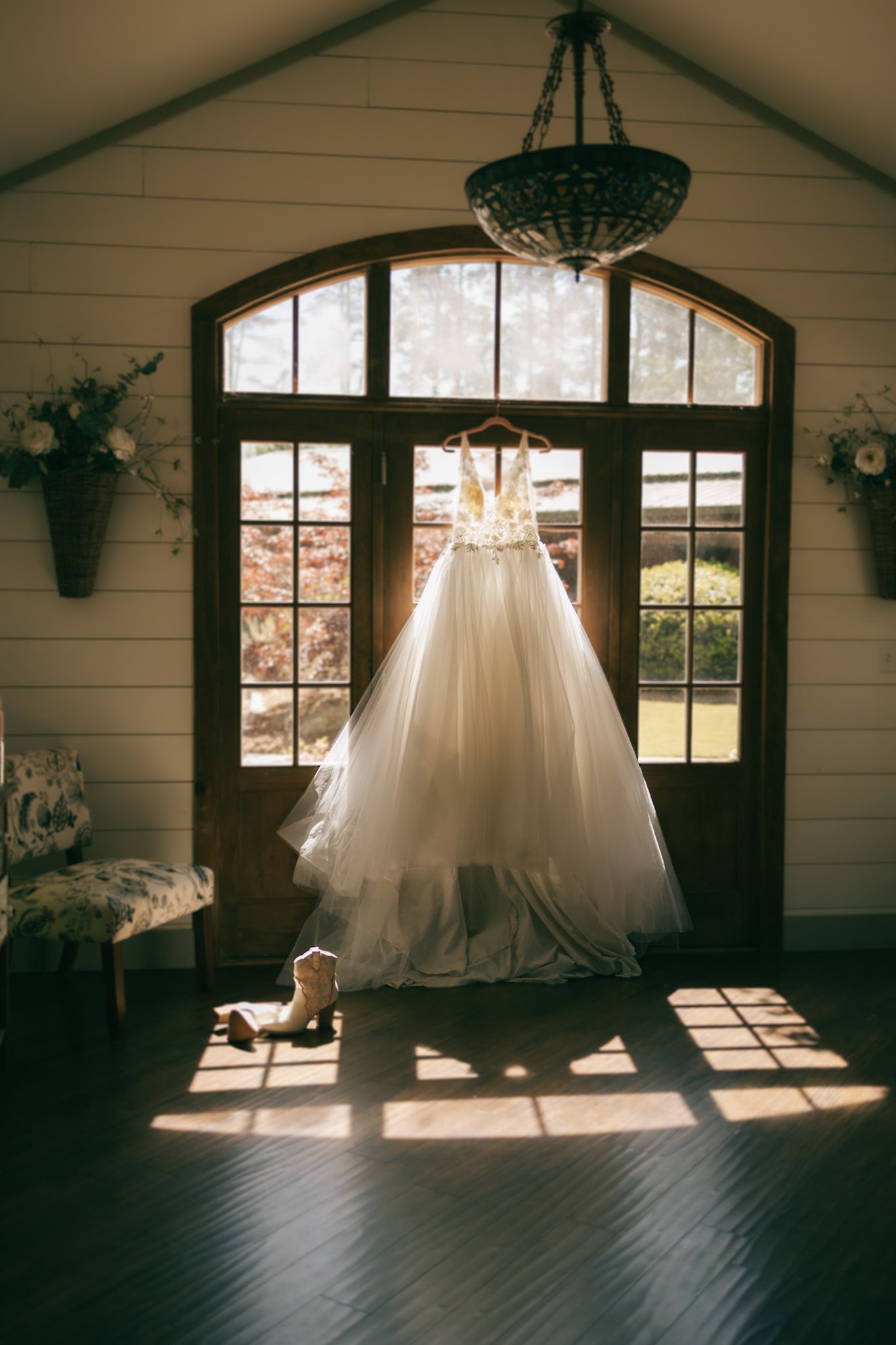 wedding gown hanging in front of the windows of the big arch of venue