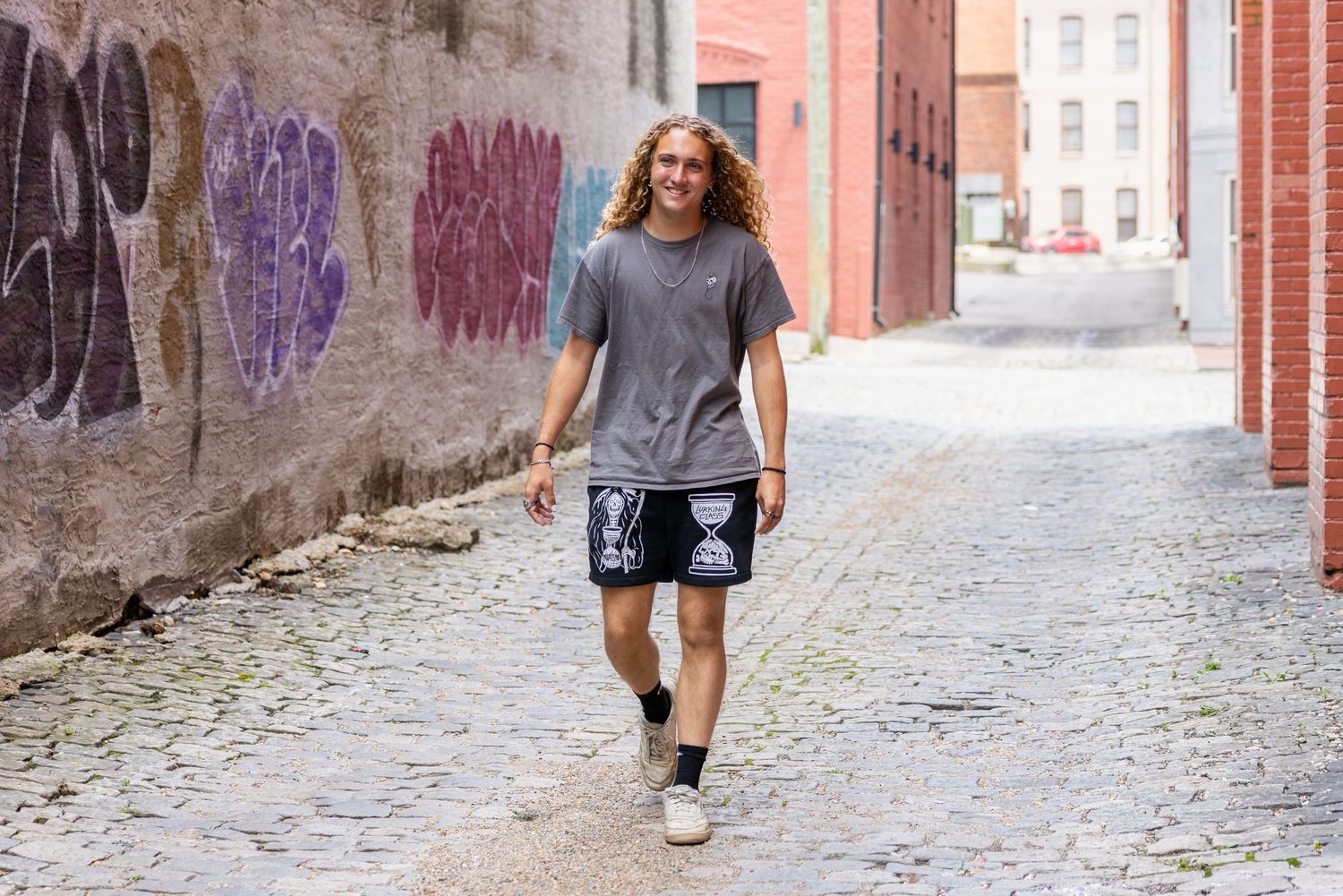 Person walking along a cobblestone path next to red brick buildings on a sunny day.