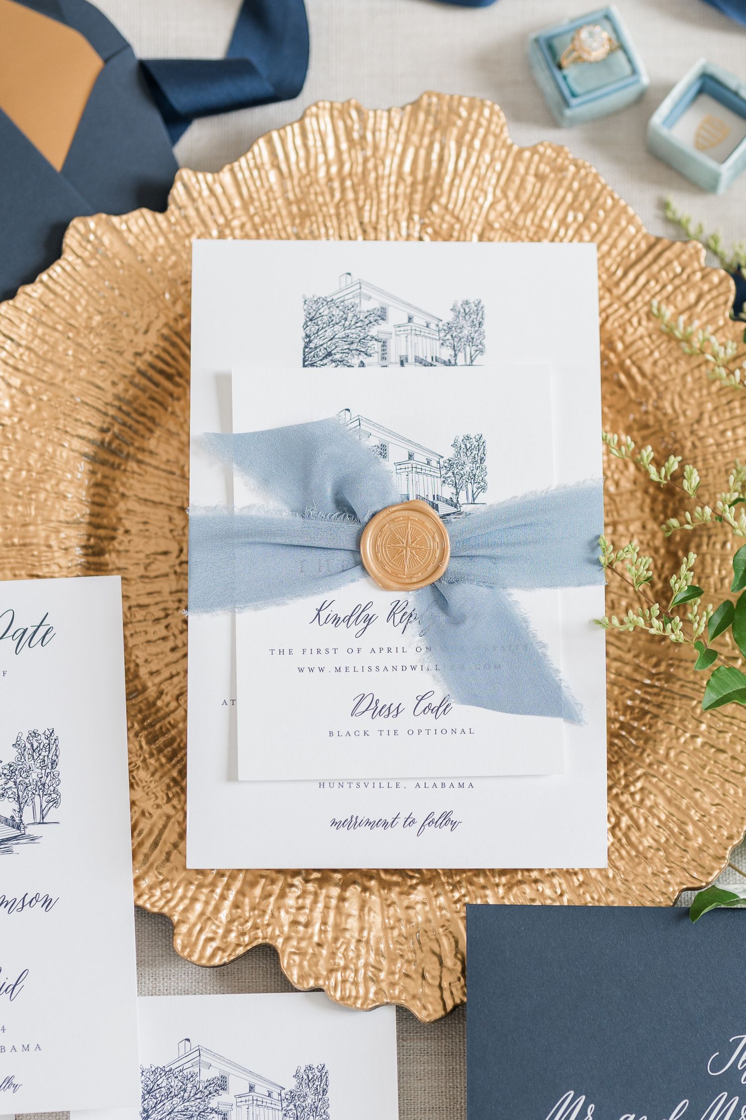 Wedding invitations with light blue ribbon on gold charger plates.