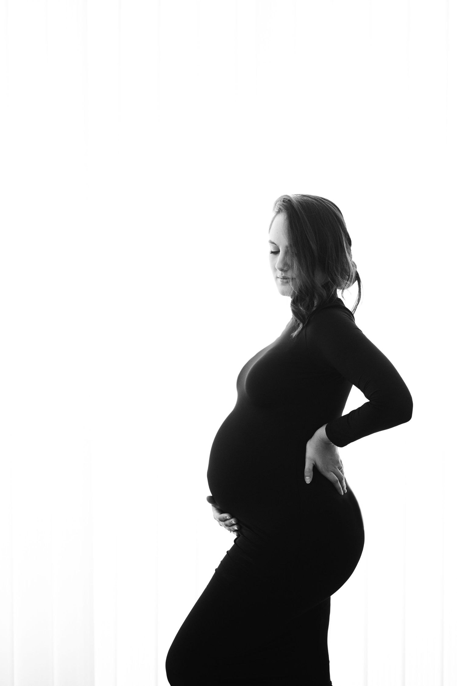 Artistic maternity photo with someone in casual denim against white wall.