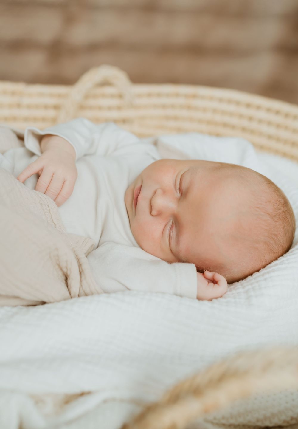 Peaceful sleeping baby in white clothing nestled in soft cream-colored bedding.