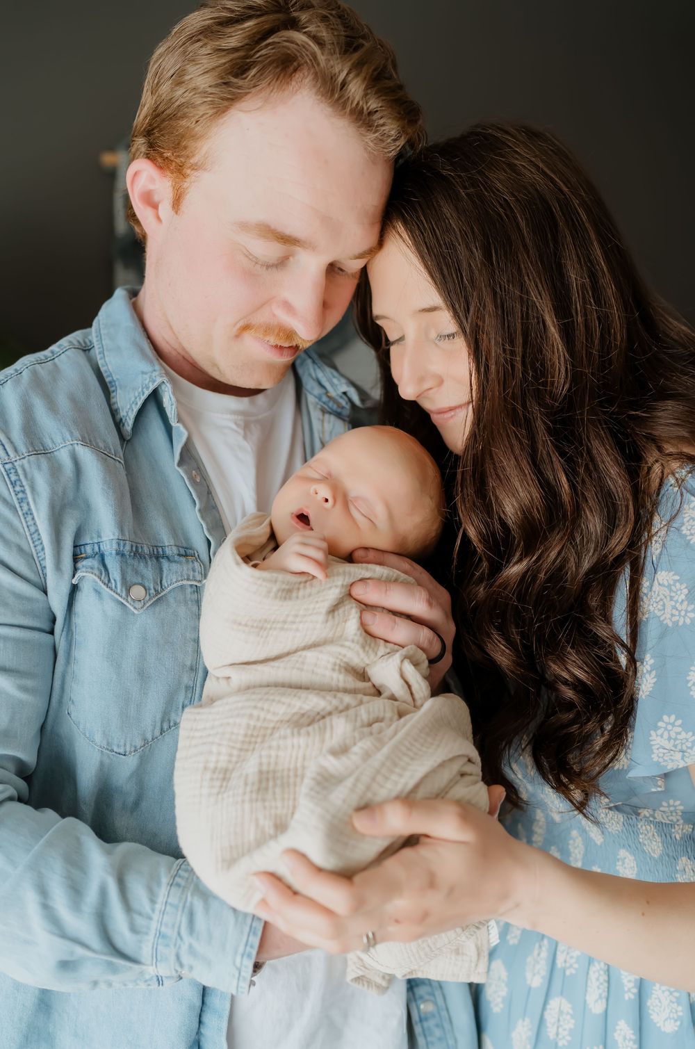 Tender family moment captured in soft lighting against dark background with denim and white clothing.