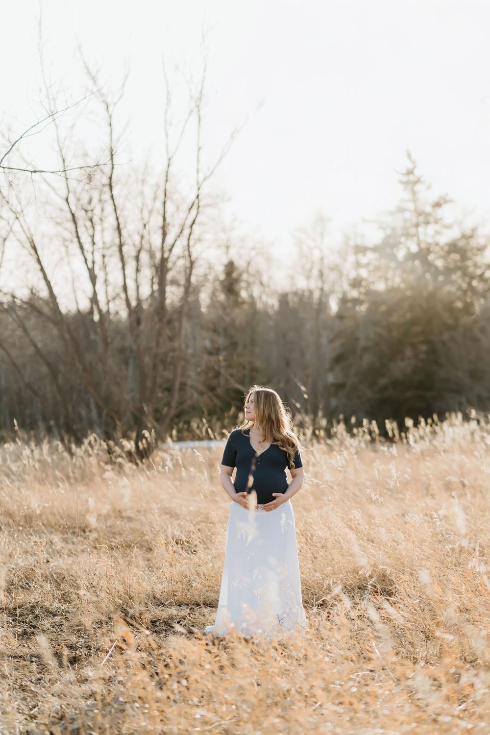 Person in white dress standing in golden tall grass field during sunset.