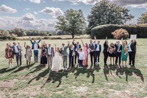 Wedding party group poses outdoors in a scenic field with trees and clouds in the background.