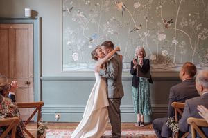 Wedding couple dancing and celebrating with guests in an elegant indoor venue with floral wallpaper.