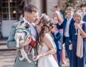 Wedding celebration moment captured with guests watching as a couple dances with their pug on the dance floor.