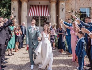 Wedding guests celebrate and throw confetti outside a rustic Italian villa with red striped awning.
