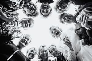 Black and white photo of wedding guests forming a circle and smiling down at the camera.