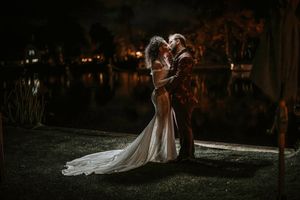 A couple in wedding attire shares an intimate moment in a garden with dramatic lighting and autumn foliage.