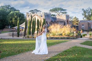 A bride in a flowing white gown poses in a garden setting with cypress trees and autumn foliage.