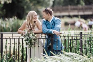 A couple shares an intimate moment on a bridge surrounded by lush greenery and white flowers in the garden.