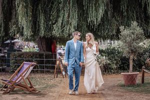 Newlyweds walking through a garden setting with weeping willow trees in the background.