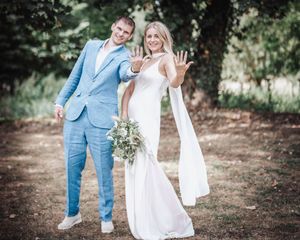 Couple in wedding attire sharing joyful moments outdoors under trees.