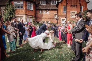 Wedding guests gather outside a brick building to celebrate as newlyweds share a joyful moment together.