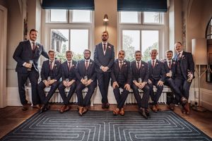 A wedding party in formal attire poses together in an elegant room with large windows and a geometric patterned rug.